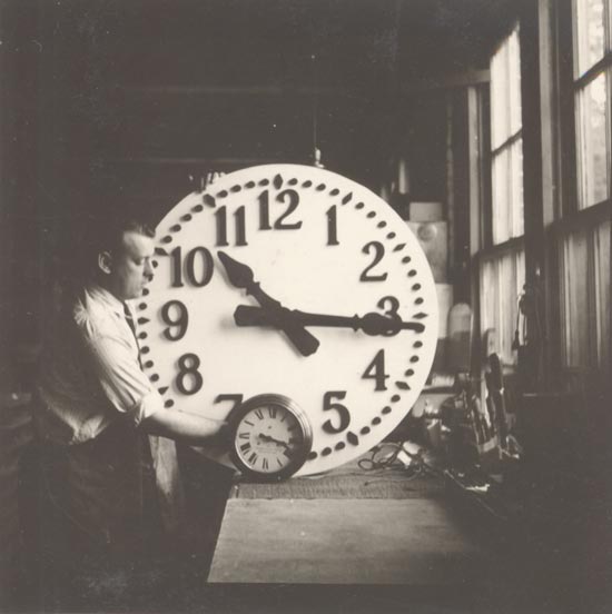 Bill Thrasher compares large and small clocks in this circa 1930 factory photo